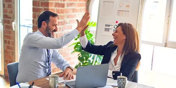 happy travel agents in office high-fiving each other after a successful business travel accommodation deal